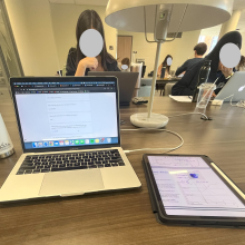 Students studying in the background, with a laptop and tablet in the foreground.